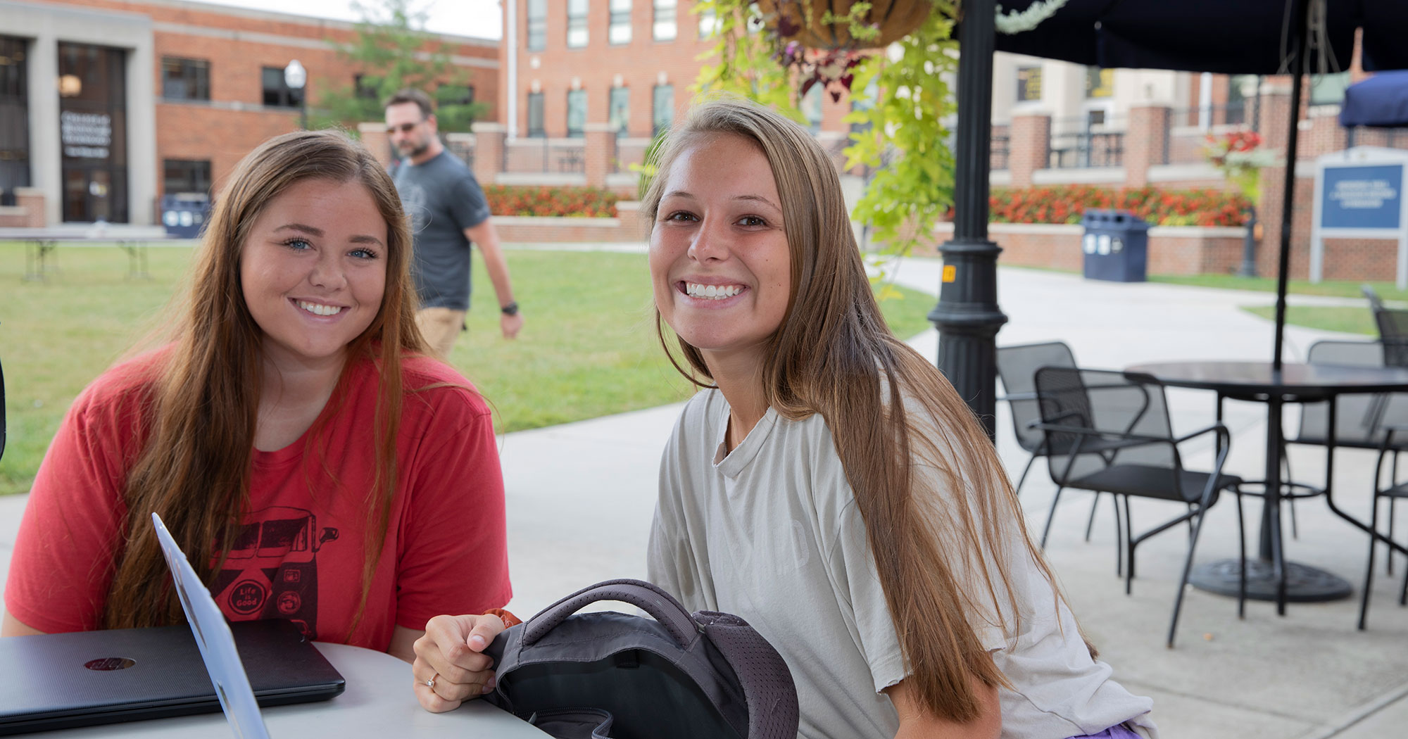 Two young women sit at a picnic table on campus. There are buildings in the background.