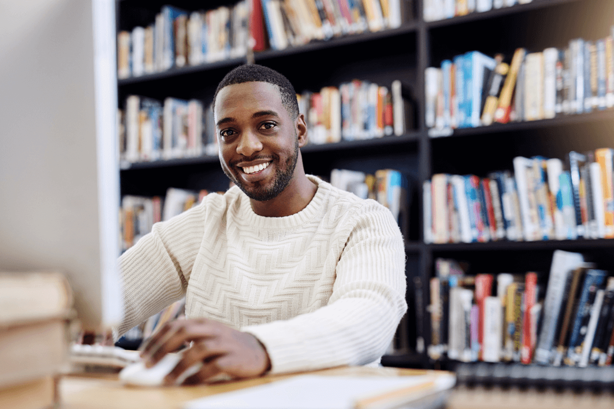 A young man sits at a computer in a library. 