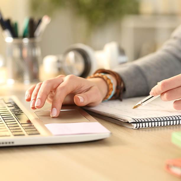 Hand using keyboard on a laptop with pen and notebook nearby