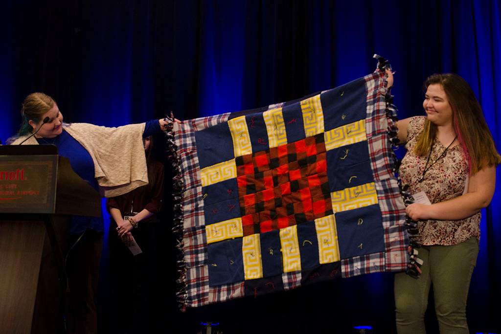 Photo of students holding a quilt on stage