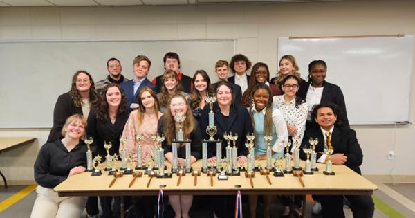 Speech and Debate team stand behind a table with a lot of trophies