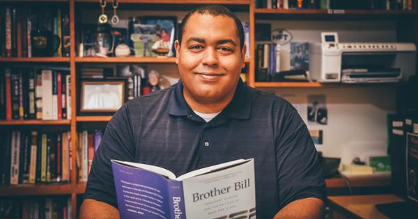 Dr. Daryl Carter sitting in front of rows of bookshelves and holding an open book in his hands