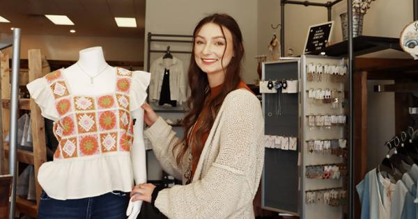 A student smiles at you with their custom clothing on display on a dress form.