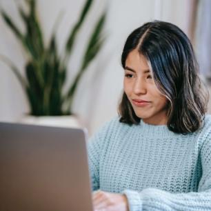 Student wearing a blue sweater while facing a laptop computer.