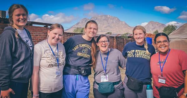 Dr. Emily Flores poses for a photo with several students during a trip to Malawi in May, with mountains visible in the background. 