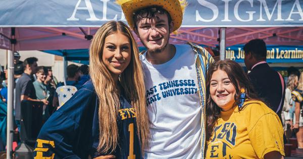 A group of three ETSU students at a tailgating event decked out in blue and gold gear