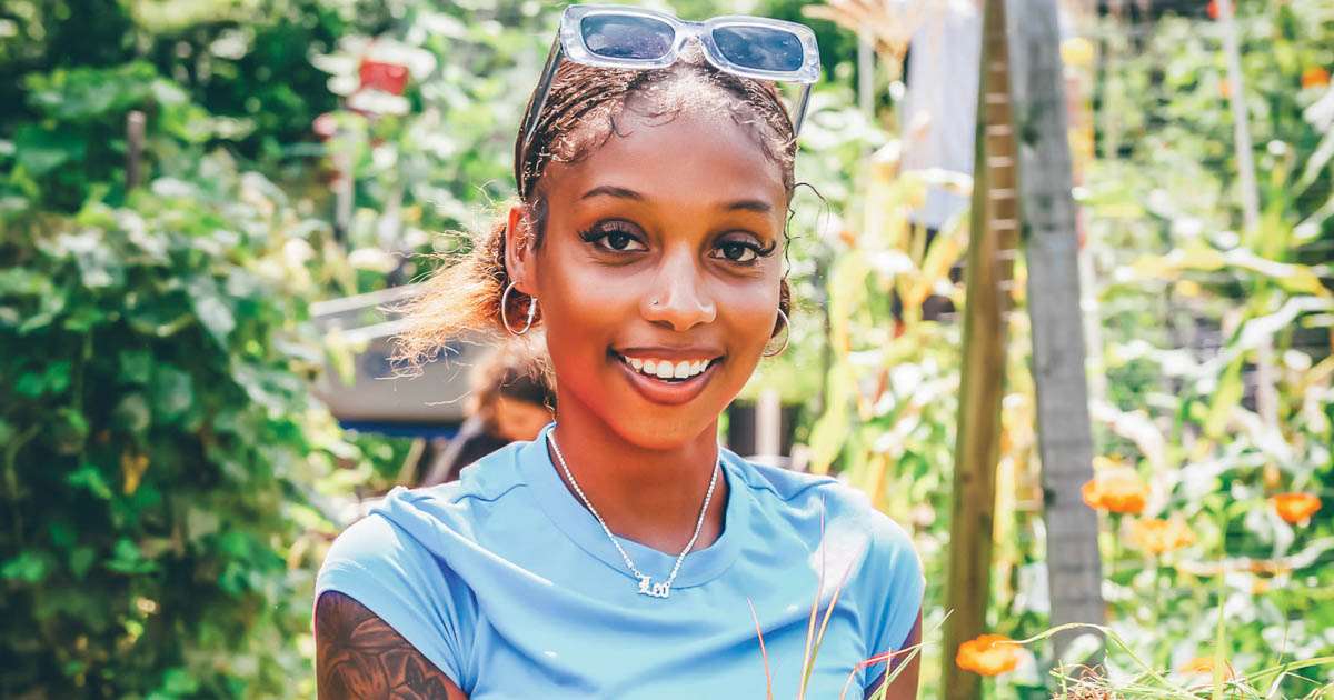 A student holding weeds she has just picked in a garden.