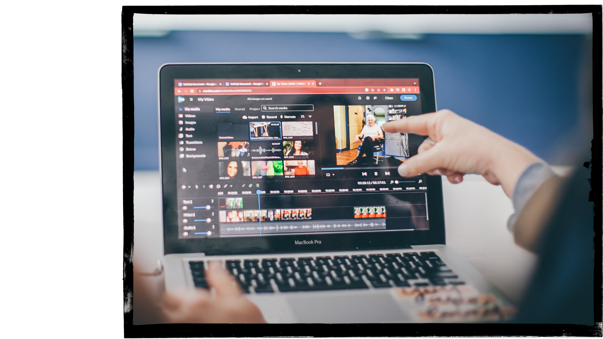 A finger points to a computer screen with video editing taking place.