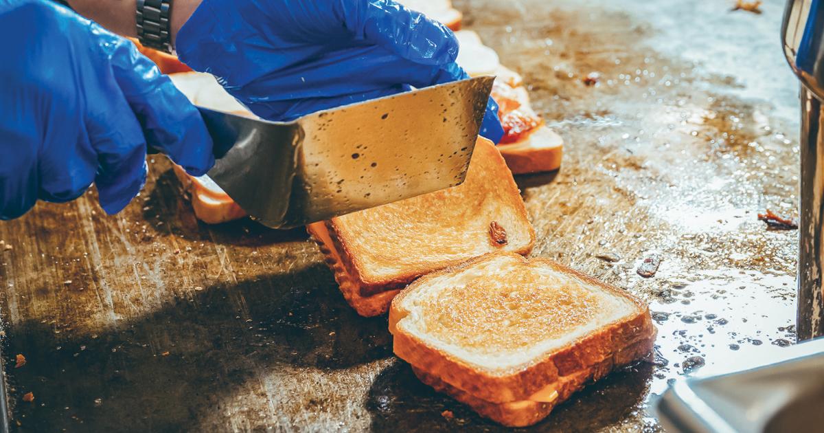 A hand holding a spatula and grilling a sandwich