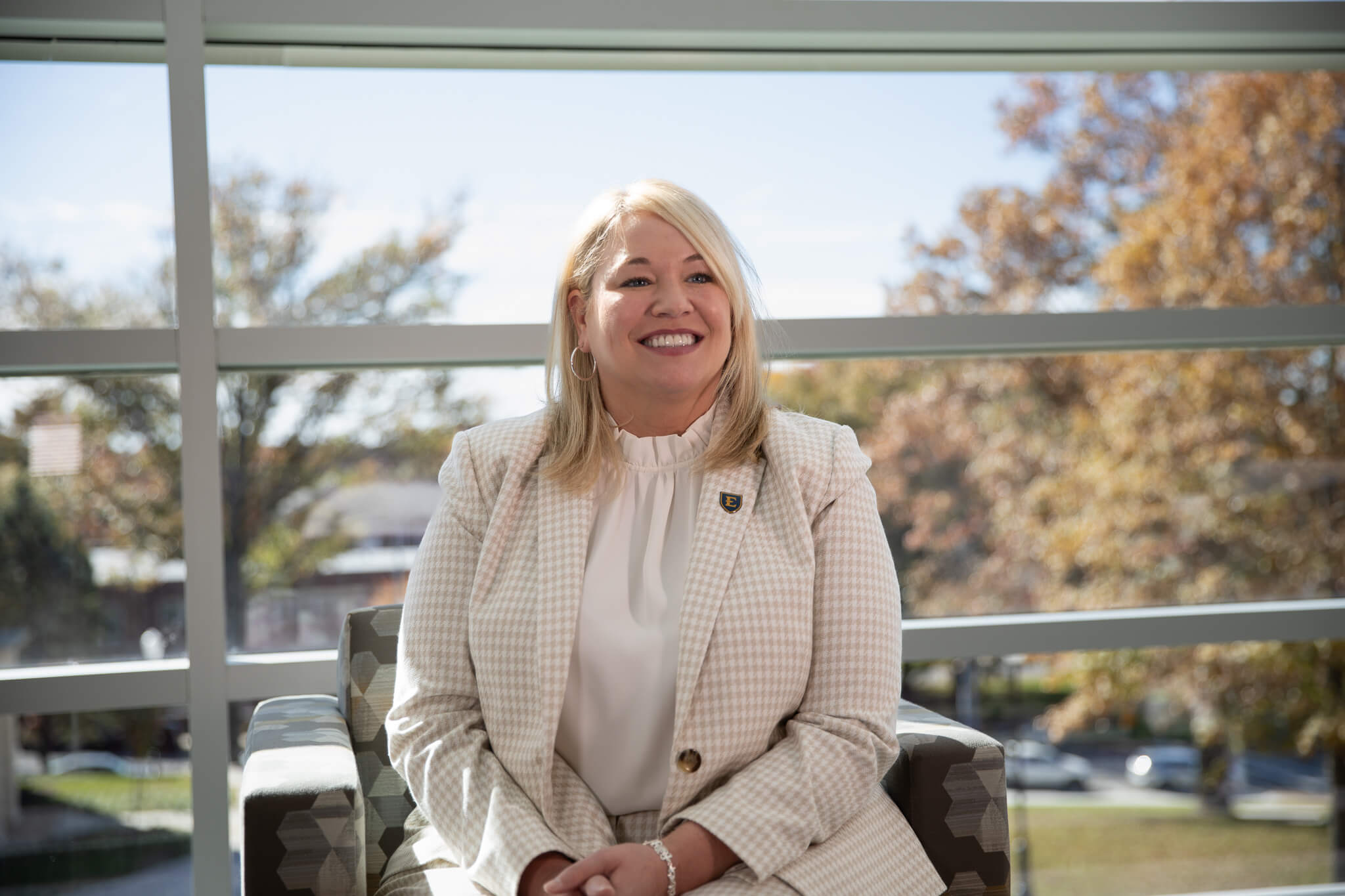 Brandi Townsley poses on a chair. She is sitting in one of the newly rennovated Lamb Hall seating areas with big windows in the background.