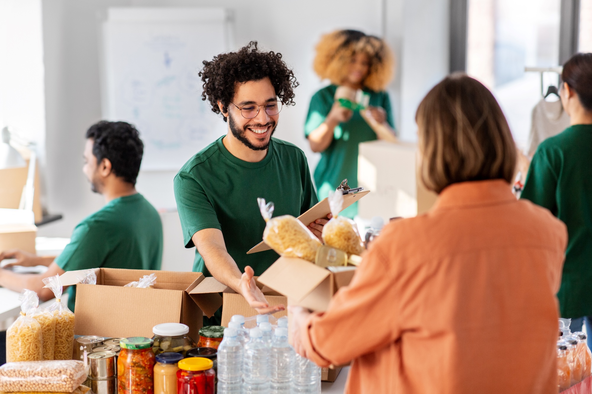 happy smiling male volunteer with clipboard and woman taking box of food.