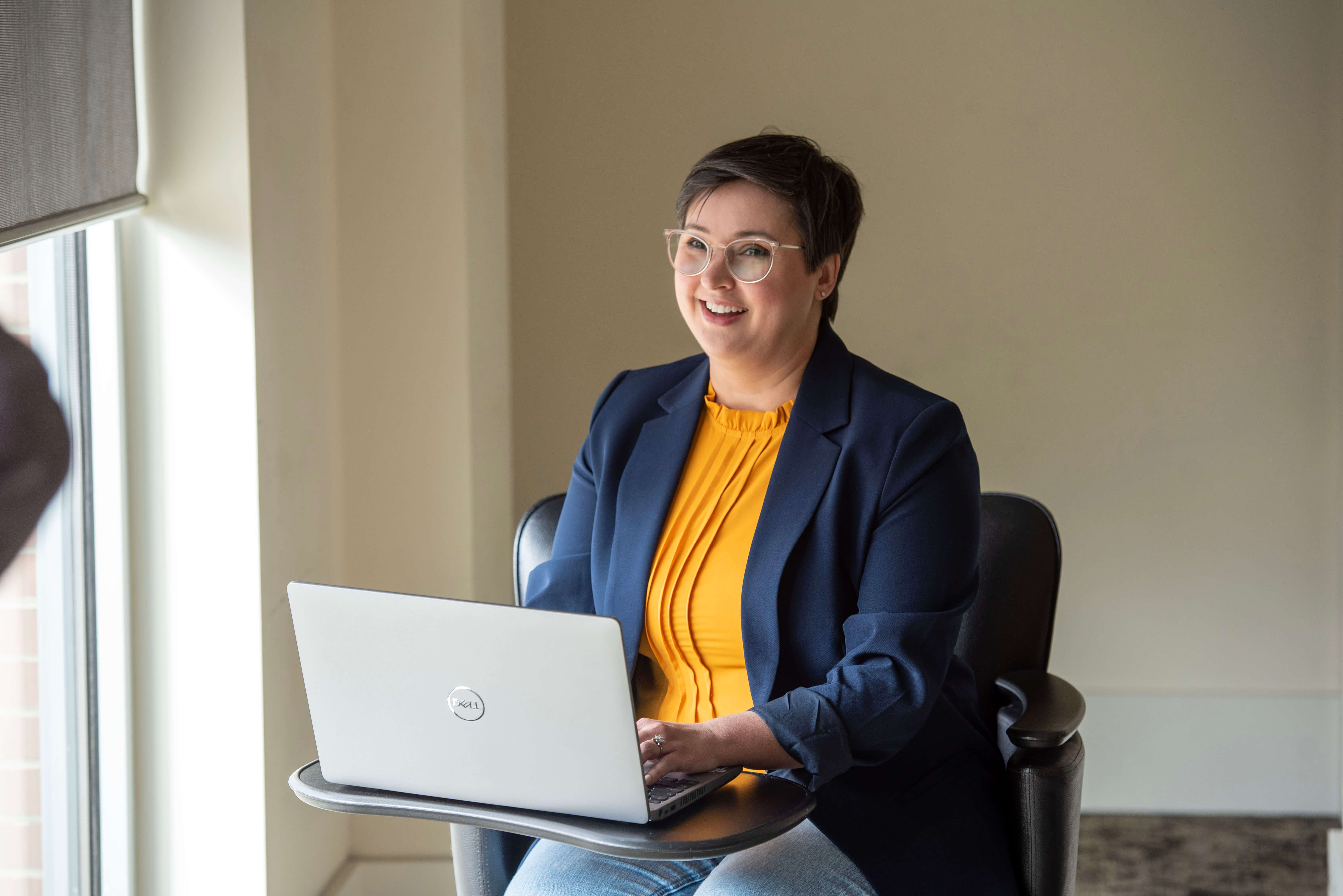 A woman sits with her latop open near a window. 