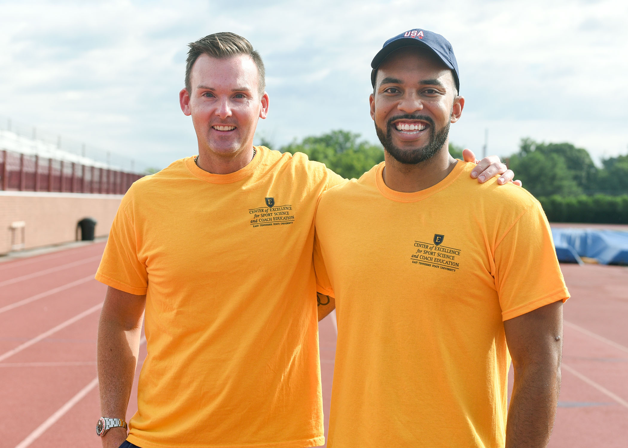 two men stand side by side on an athletic track.