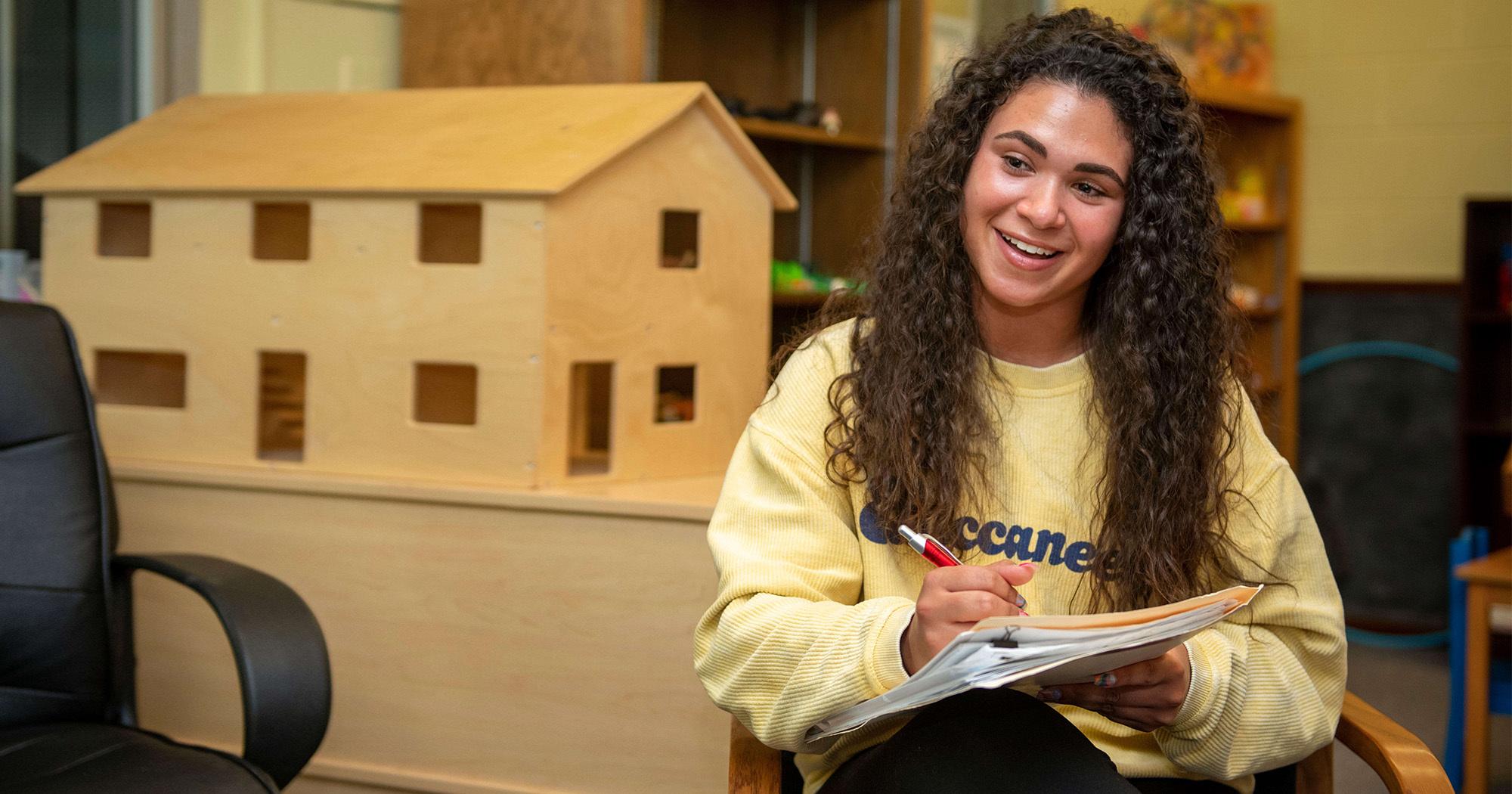 A young woman sits with a clipboard in a counseling room.