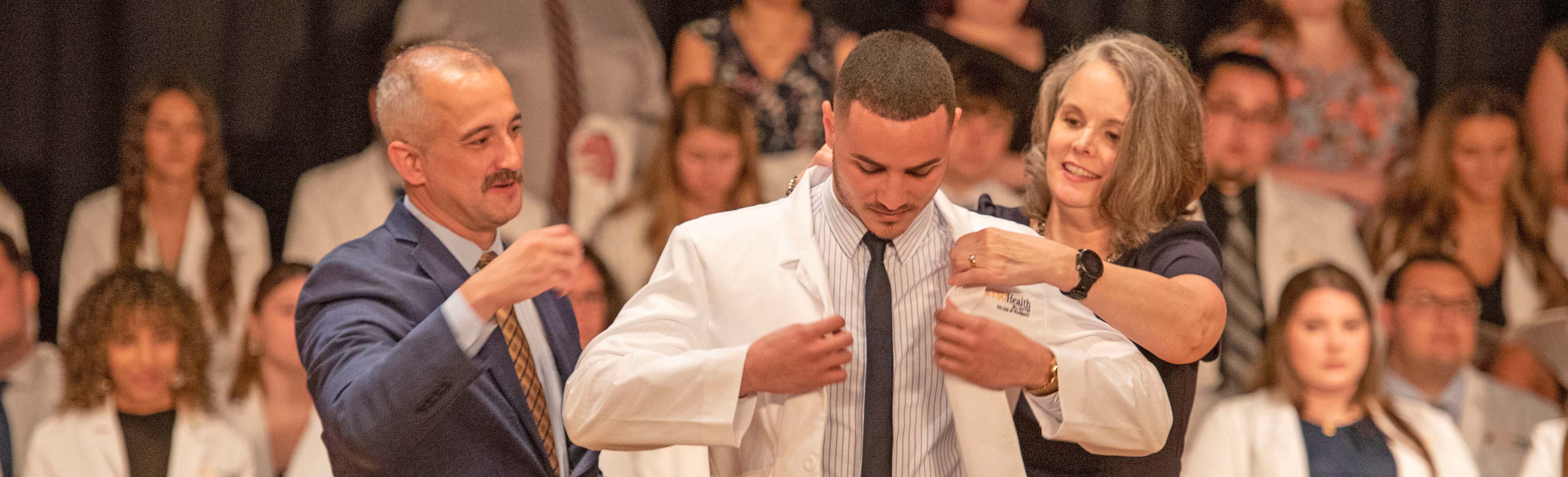 Student being given his white coat by Dean and TPA CEO.