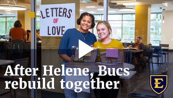 YouTube thumbnail depicting two students smiling as they write letters of love to first responders. The text reads "Using drone technology to map the damage. The text reads "After Helene, Bucs Rebuild Together."