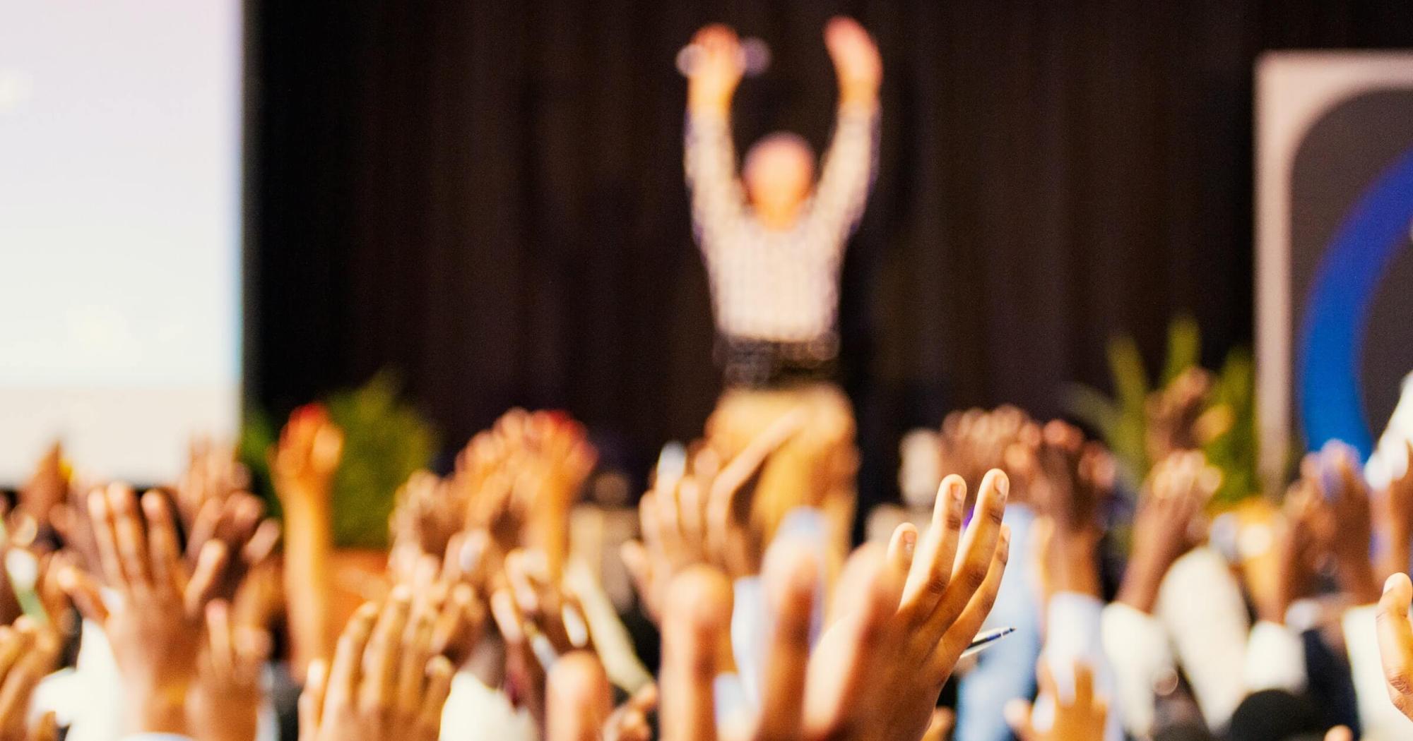 Person in front of crowd in classroom; all hands are up